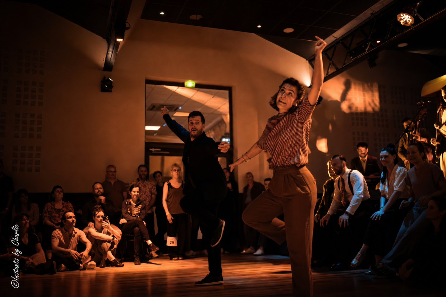 Danseuse et danseur de Lindy Hop en pleine envolée sous les lumières chaudes de la salle